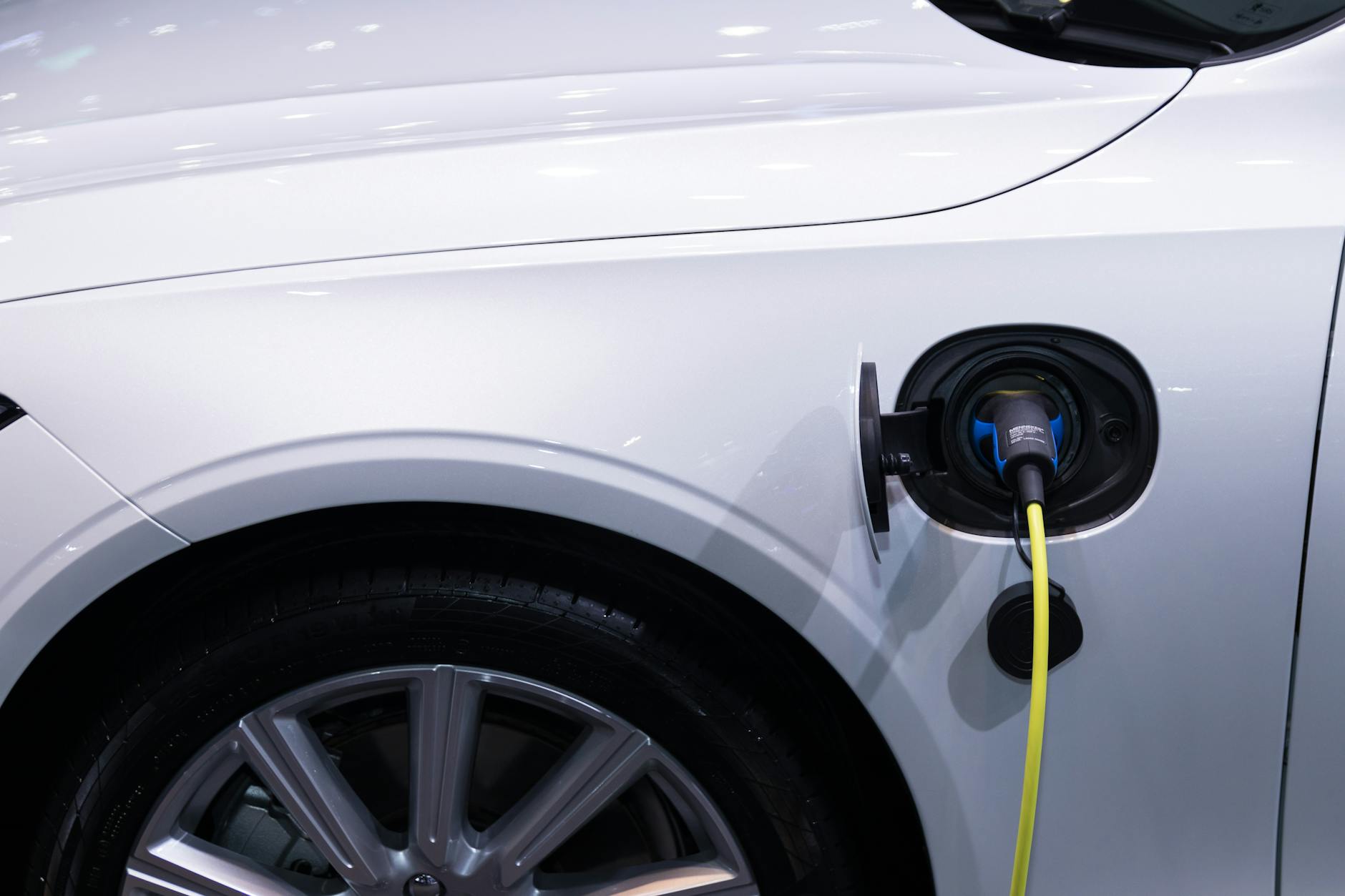 Biały samochód elektryczny ładowany przez kabel, zbliżenie na gniazdo